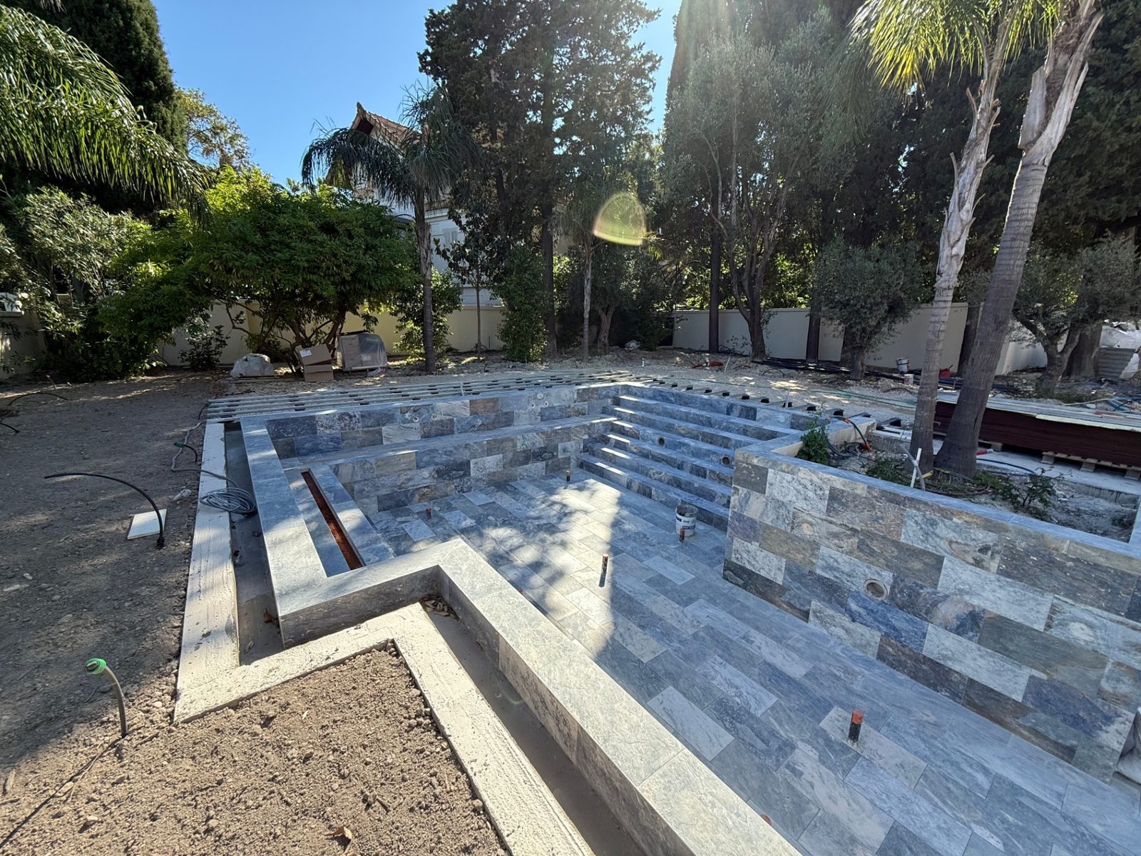 Piscine miroir en cours de finition : carrelage pierre, banquette, escalier et goulotte de débordement
