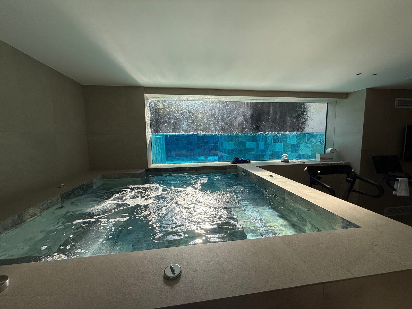 Spa intérieur en pierre avec vue sur le bassin de la piscine à travers une baie vitrée